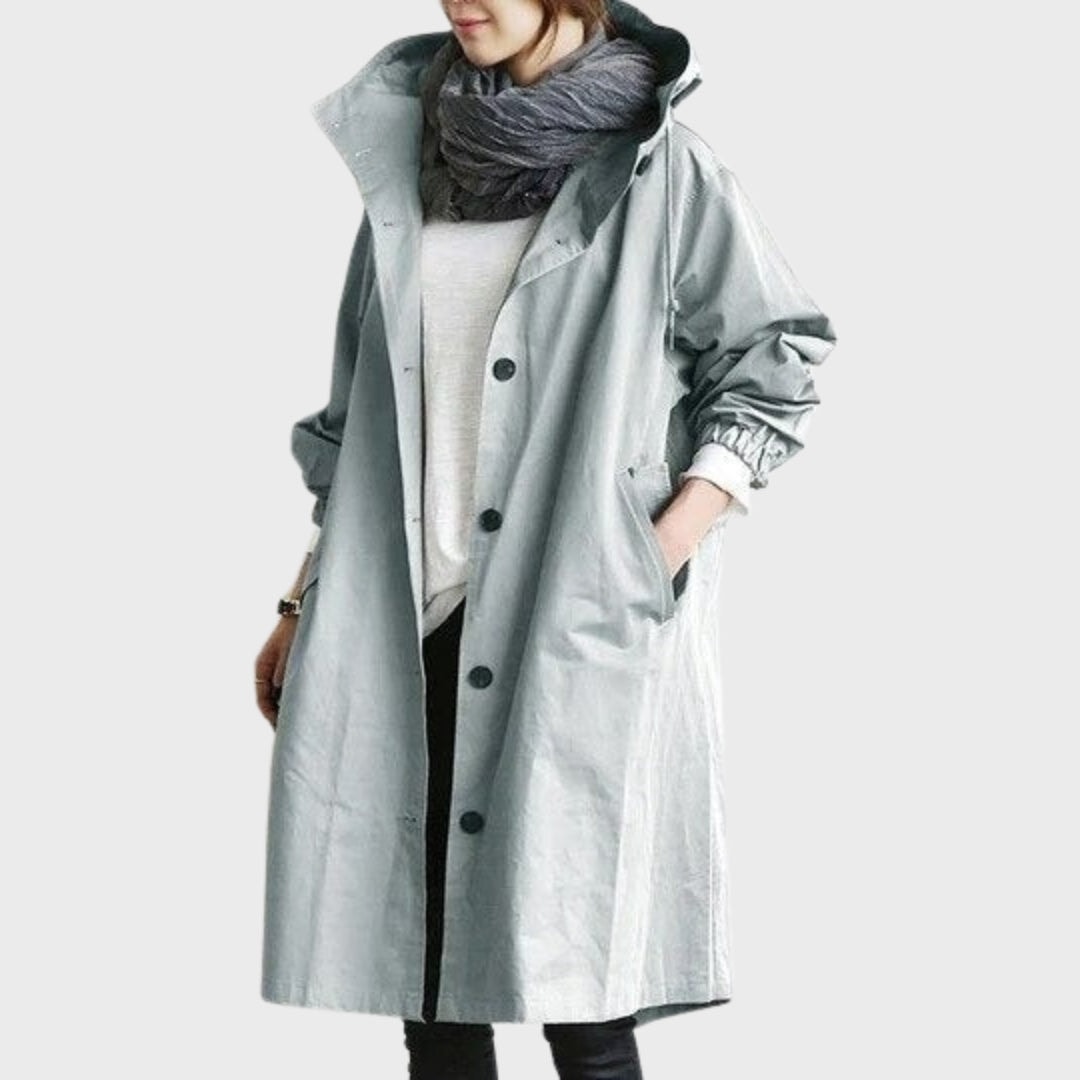 Gabardina larga gris muy claro con capucha, bolsillos laterales y puños elásticos en las mangas.