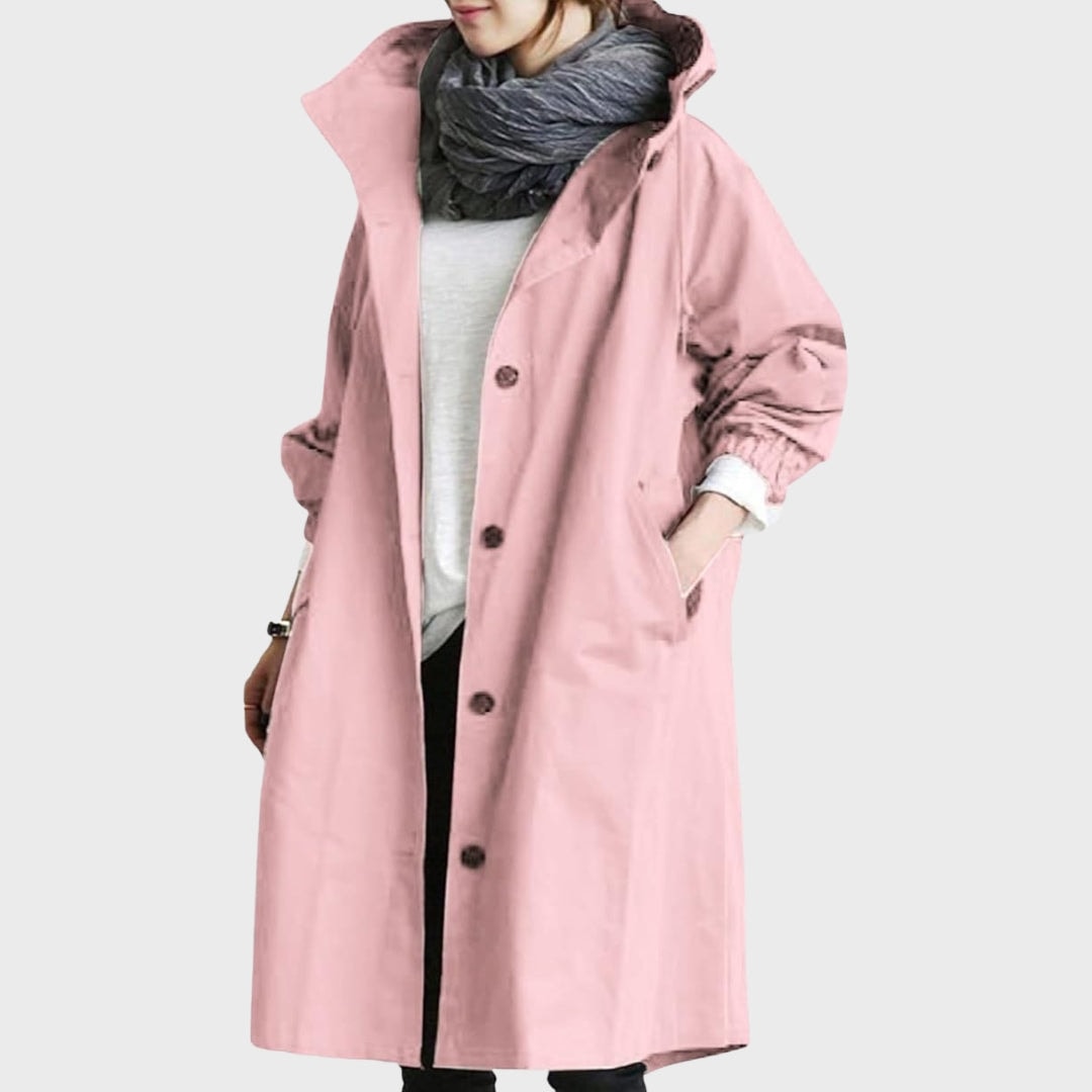 Gabardina larga rosa con capucha, botones oscuros y bolsillos laterales, llevada sobre un conjunto claro.