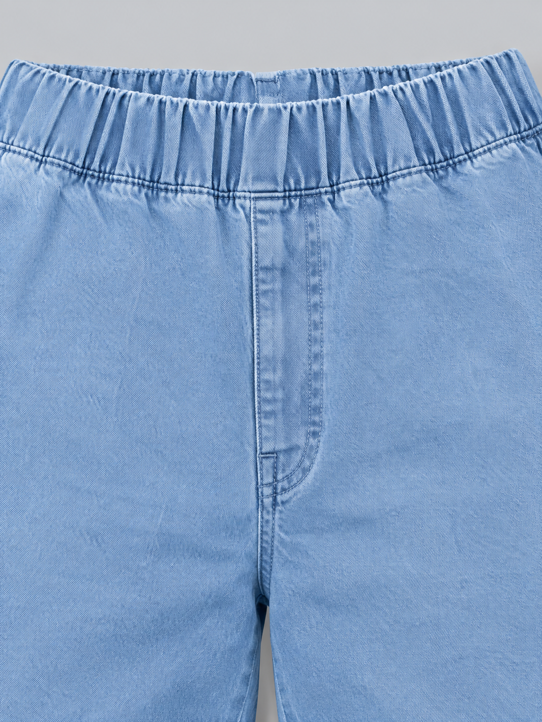 Primer plano de la cintura elástica fruncida y la costura central delantera de los jeans azul claro.