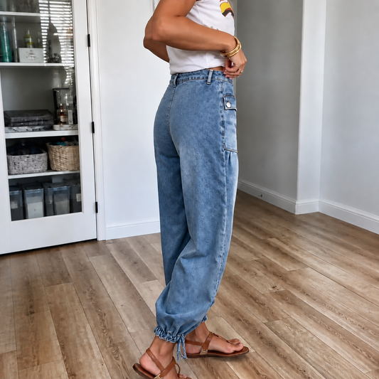 Vista lateral de jeans azules de pierna curva con bolsillos laterales y bajo fruncido mediante lazos ajustables.