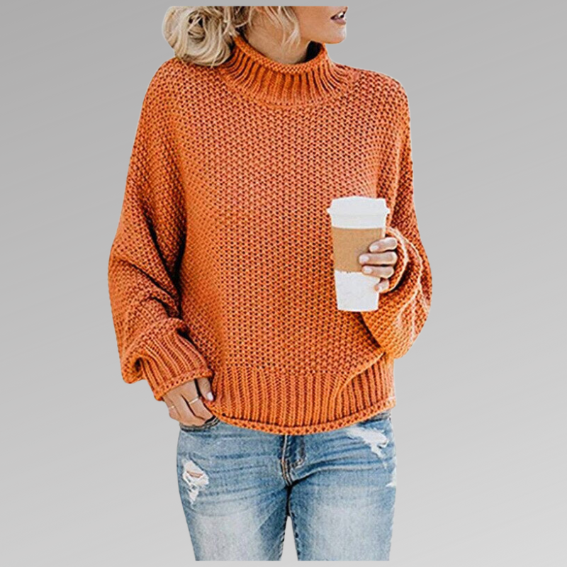 Jersey naranja de cuello alto, corte holgado y mangas amplias, combinado con vaqueros mientras la modelo sostiene un vaso de café.