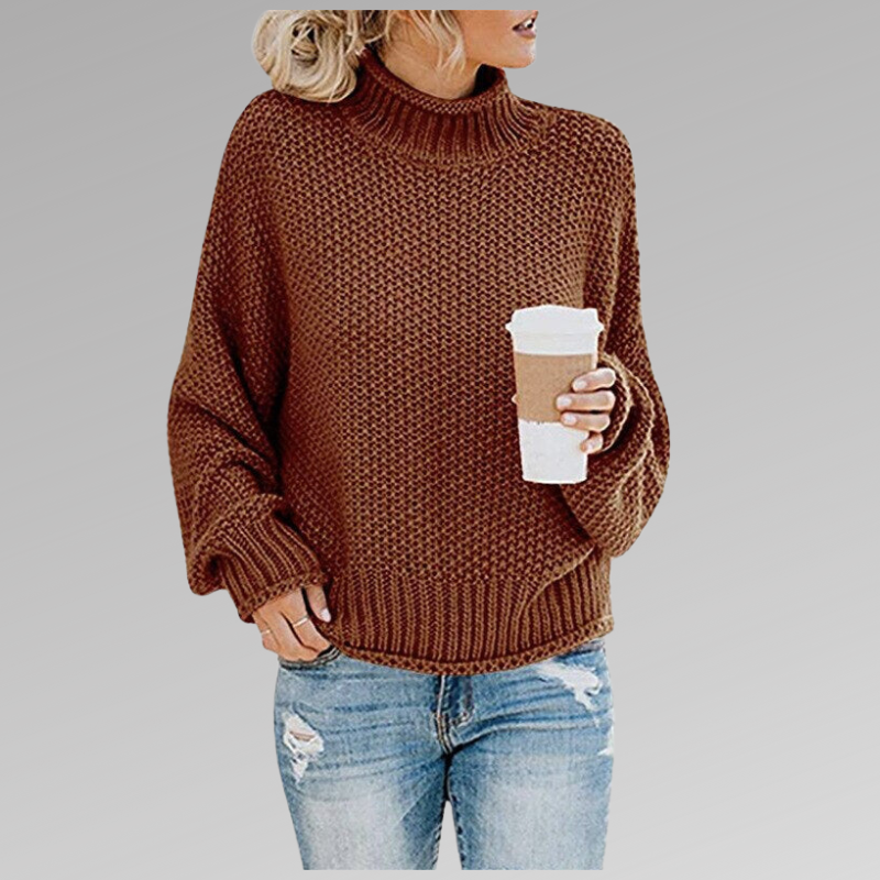 Jersey marrón rojizo de cuello alto con mangas sueltas y textura de punto, combinado con vaqueros desgastados.