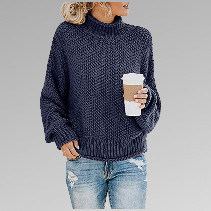Jersey azul marino de cuello alto con silueta holgada y puños acanalados, mientras la modelo sostiene un vaso.