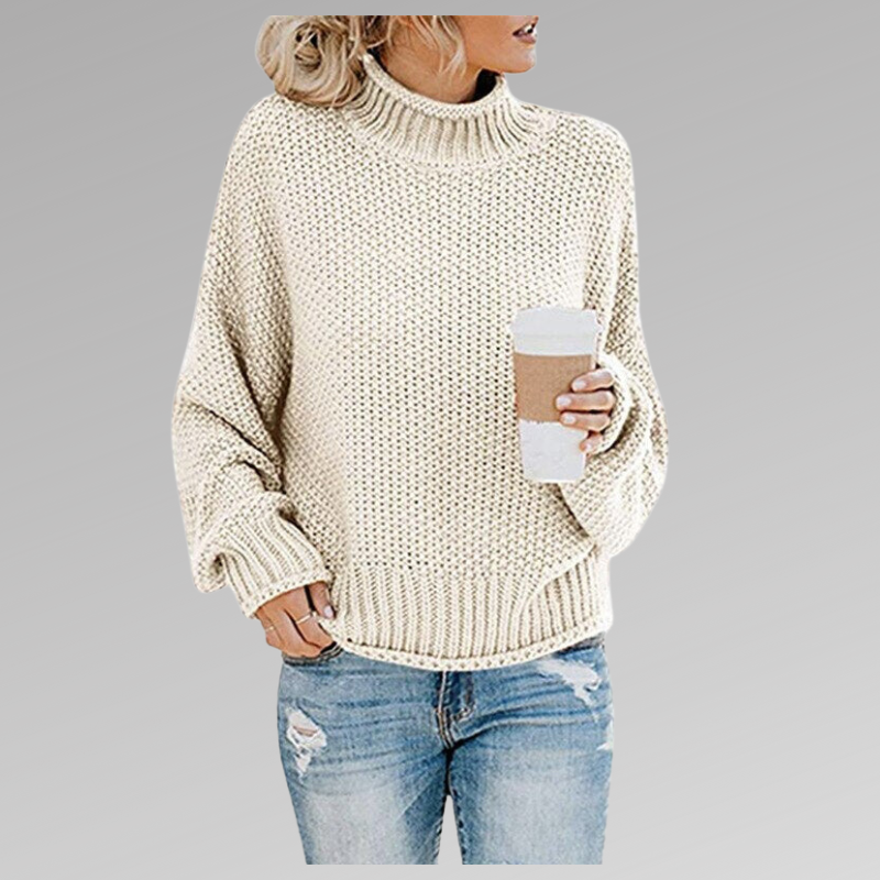 Jersey crema de cuello alto y corte relajado, con textura de punto y mangas amplias sobre vaqueros.