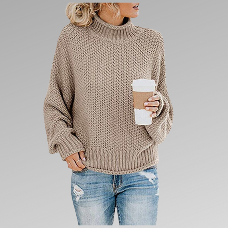 Jersey beige topo de cuello alto con bajo acanalado y volumen holgado, combinado con vaqueros de aspecto desgastado.