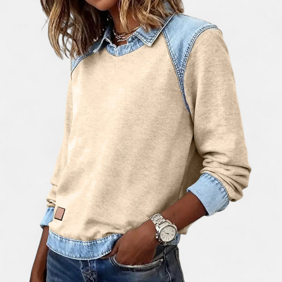 Jersey beige claro de manga larga con detalles azul claro en cuello, hombros, puños y bajo, visto desde un ángulo lateral.