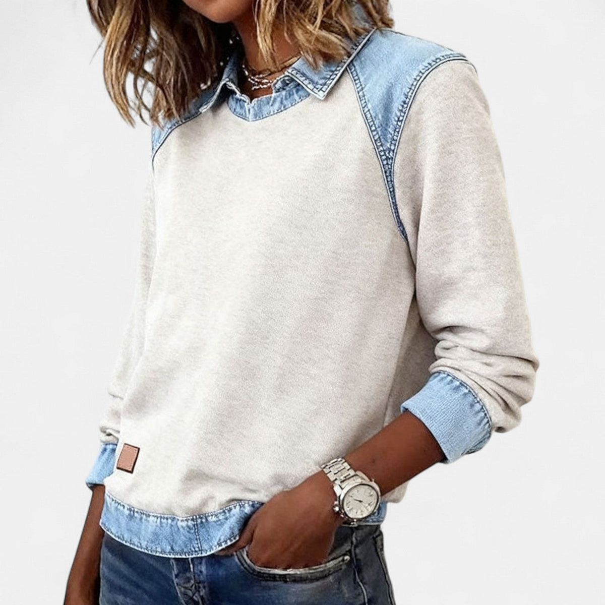 Jersey beige de mujer con efecto camisa superpuesta, mostrado en una vista frontal ligeramente lateral con un bolsillo de vaqueros.
