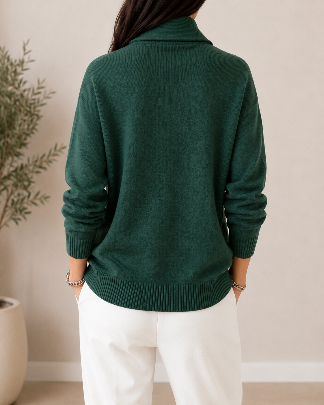 Vista posterior del jersey verde oscuro, con espalda lisa, cuello chal elevado y bajo acanalado sobre pantalón blanco.