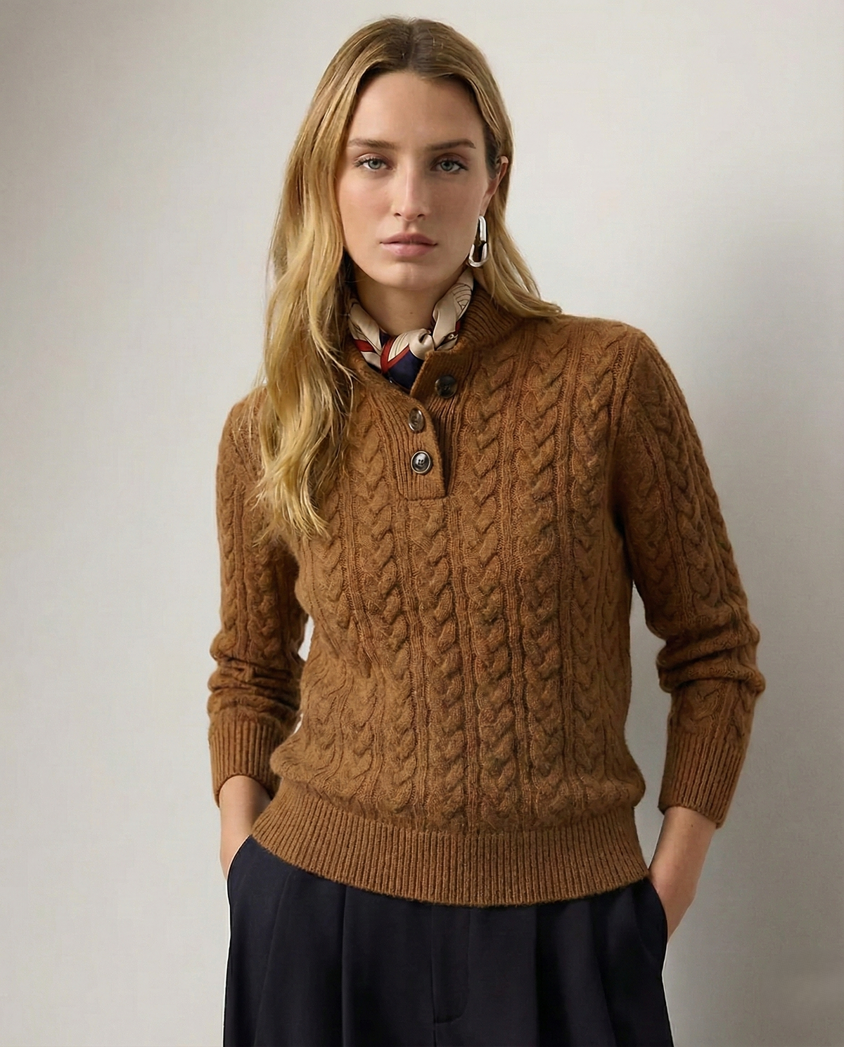 Modelo con jersey marrón de punto trenzado, cuello alto abotonado y puños acanalados, combinado con pantalón oscuro.