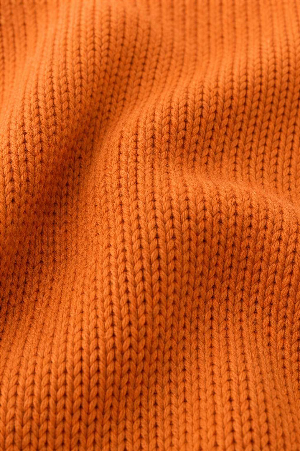 Primer plano de la textura tejida y los relieves verticales del jersey naranja.