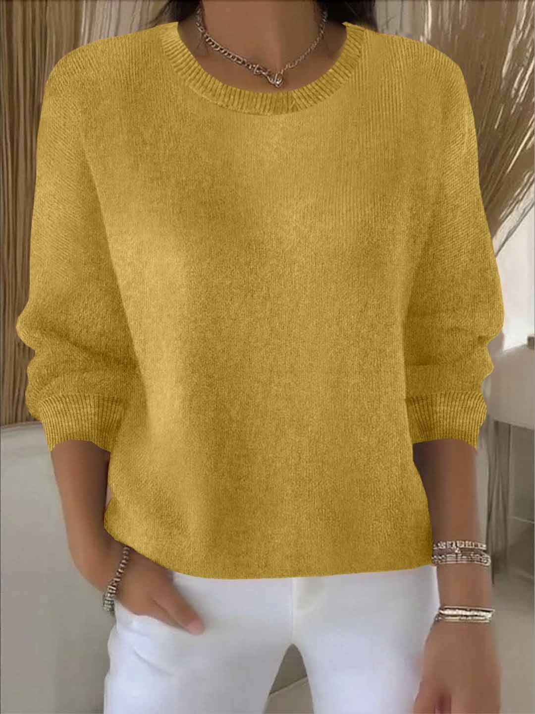 Jersey holgado amarillo mostaza de cuello redondo y mangas largas, combinado con pantalón blanco.