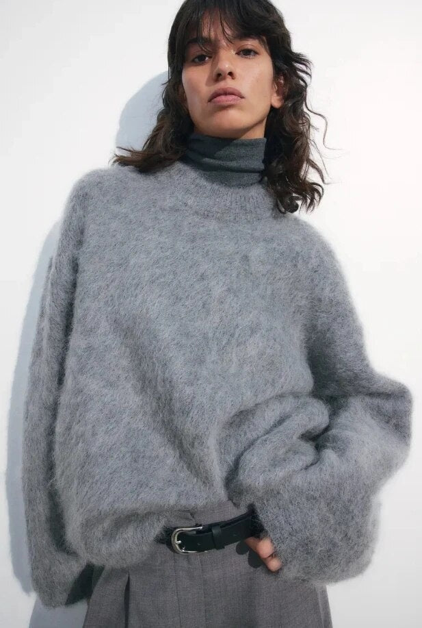 Jersey gris de silueta amplia y mangas voluminosas, mostrado con cuello redondo y un puño ancho doblado.