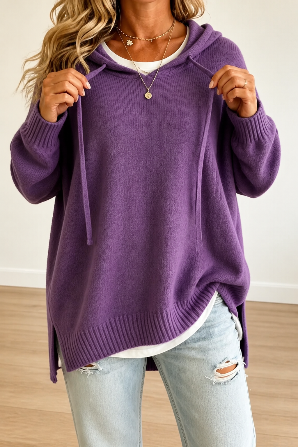 Jersey oversize morado con capucha, cordones y aberturas laterales que dejan ver la prenda blanca inferior.