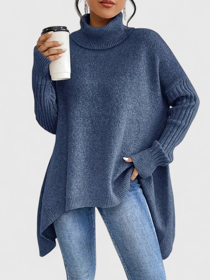 Jersey oversize azul de cuello alto, mangas largas de puño acanalado y bajo asimétrico más largo en la parte posterior, combinado con vaqueros.