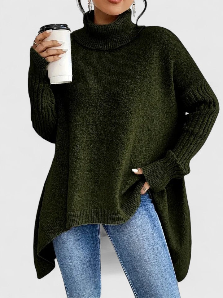 Jersey oversize verde oscuro con cuello alto y bajo asimétrico, llevado con vaqueros claros.