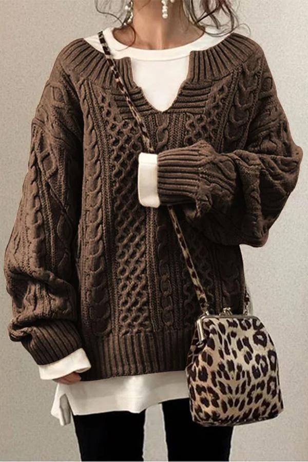 Jersey oversize de punto marrón con trenzas, cuello en V y mangas amplias, combinado con una prenda blanca debajo.