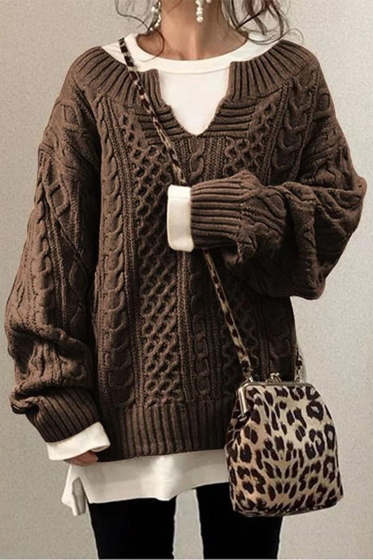 Jersey oversize de punto marrón con trenzas, cuello en V y mangas amplias, combinado con una prenda blanca debajo.
