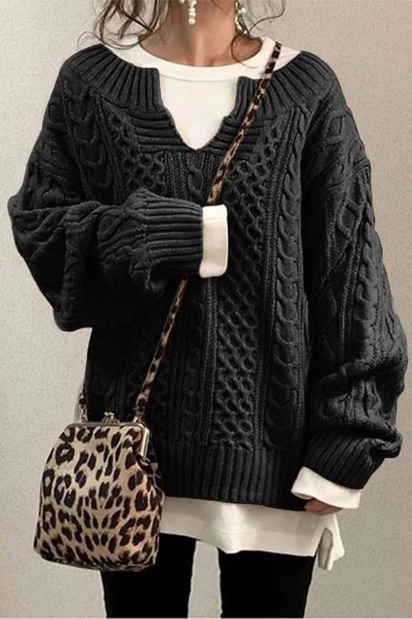 Jersey oversize negro de punto trenzado con cuello en V y mangas voluminosas, sobre una prenda blanca.