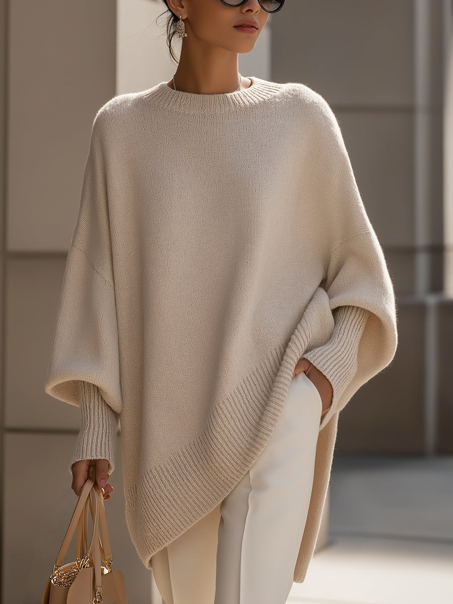 Jersey tipo poncho beige de silueta amplia, manga larga y bajo asimétrico, combinado con pantalón claro.