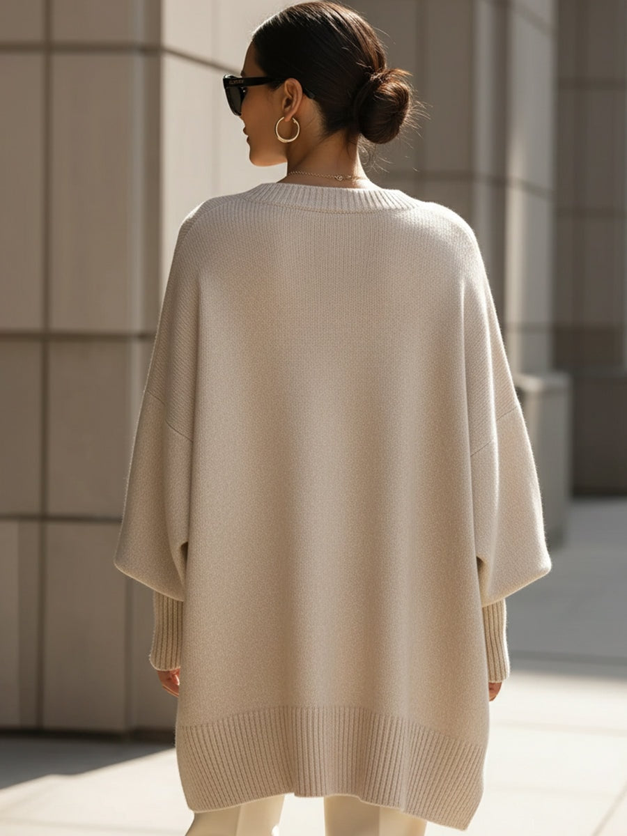 Vista posterior del jersey beige tipo poncho, con espalda amplia, mangas largas y bajo recto de canalé.