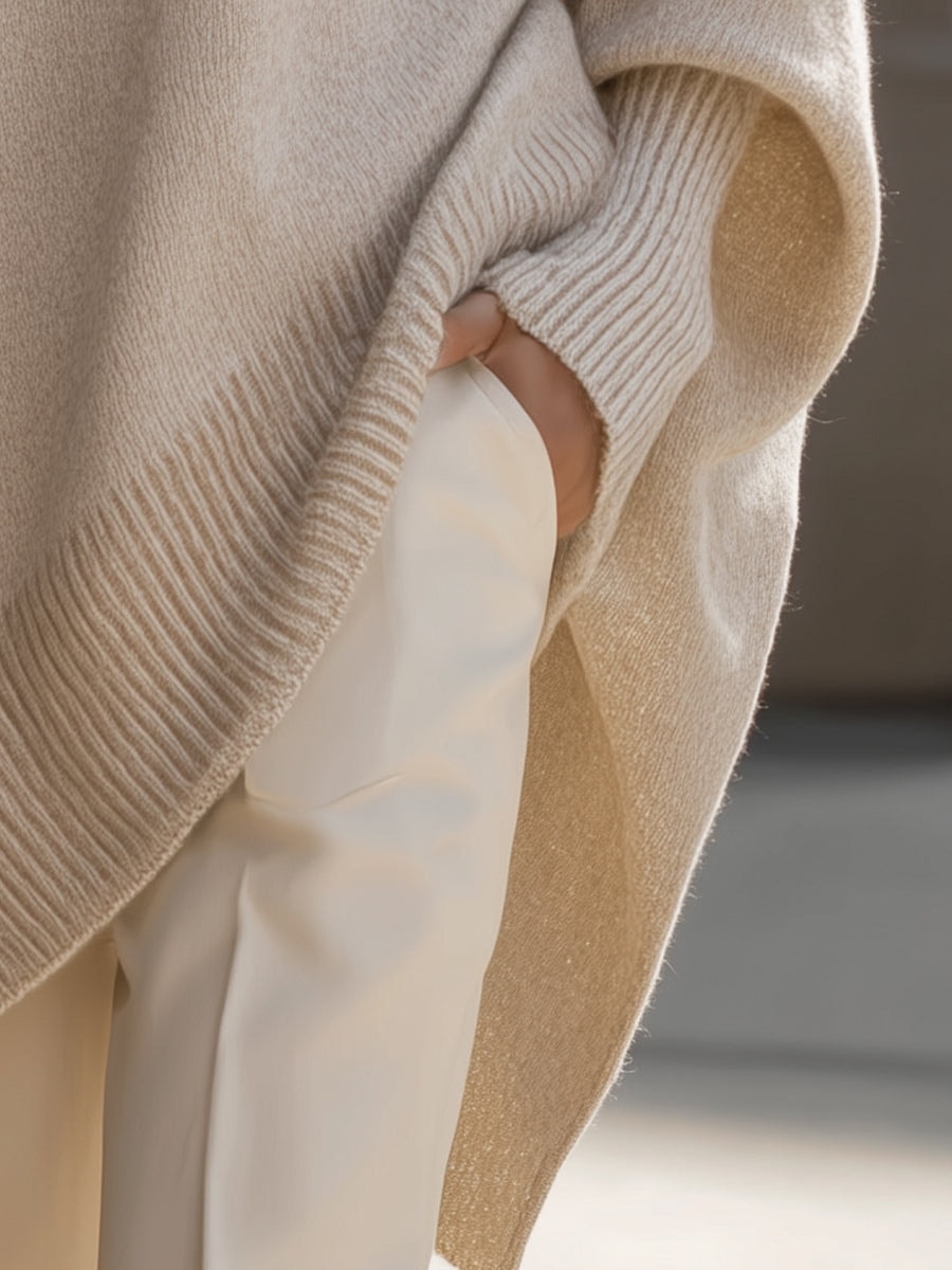 Detalle lateral del jersey beige mostrando el bajo alargado y asimétrico junto al pantalón claro.