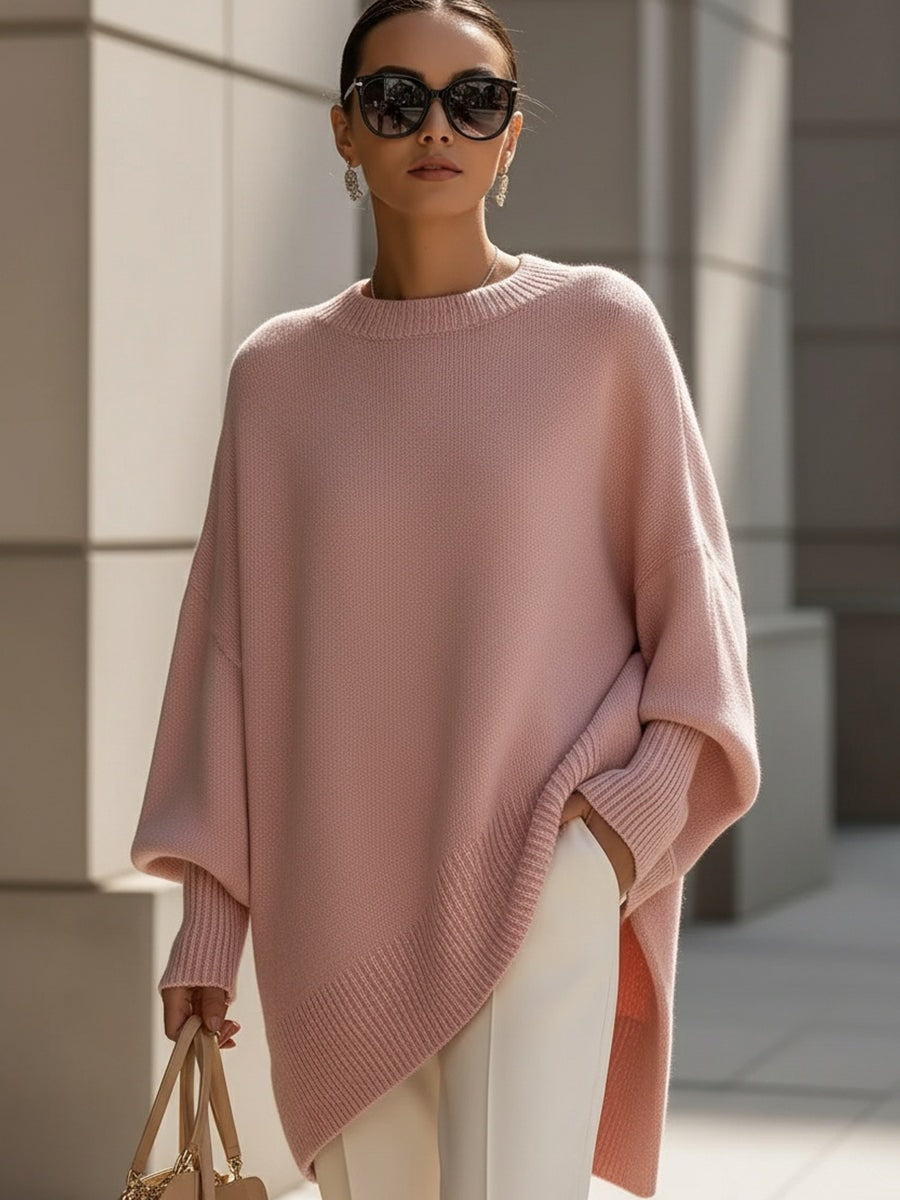 Jersey tipo poncho rosa con mangas largas, cuello redondo y bajo asimétrico, llevado con pantalón claro.