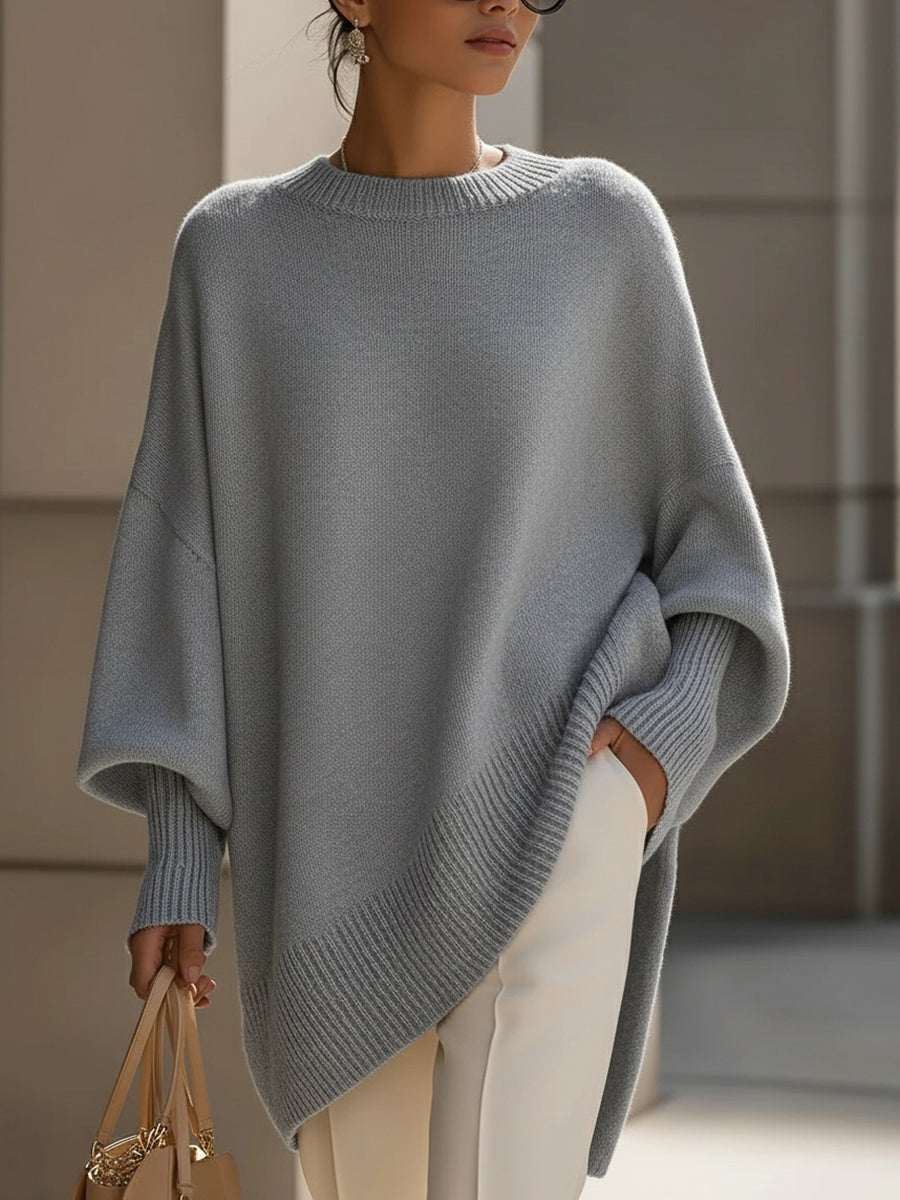 Jersey tipo poncho gris con mangas largas amplias, cuello redondo y bajo asimétrico.