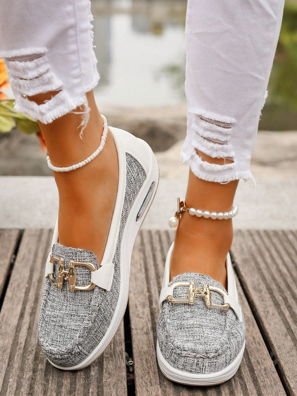Mocasines gris jaspeado con plataforma blanca y detalle metálico dorado, vistos sobre una superficie de madera.