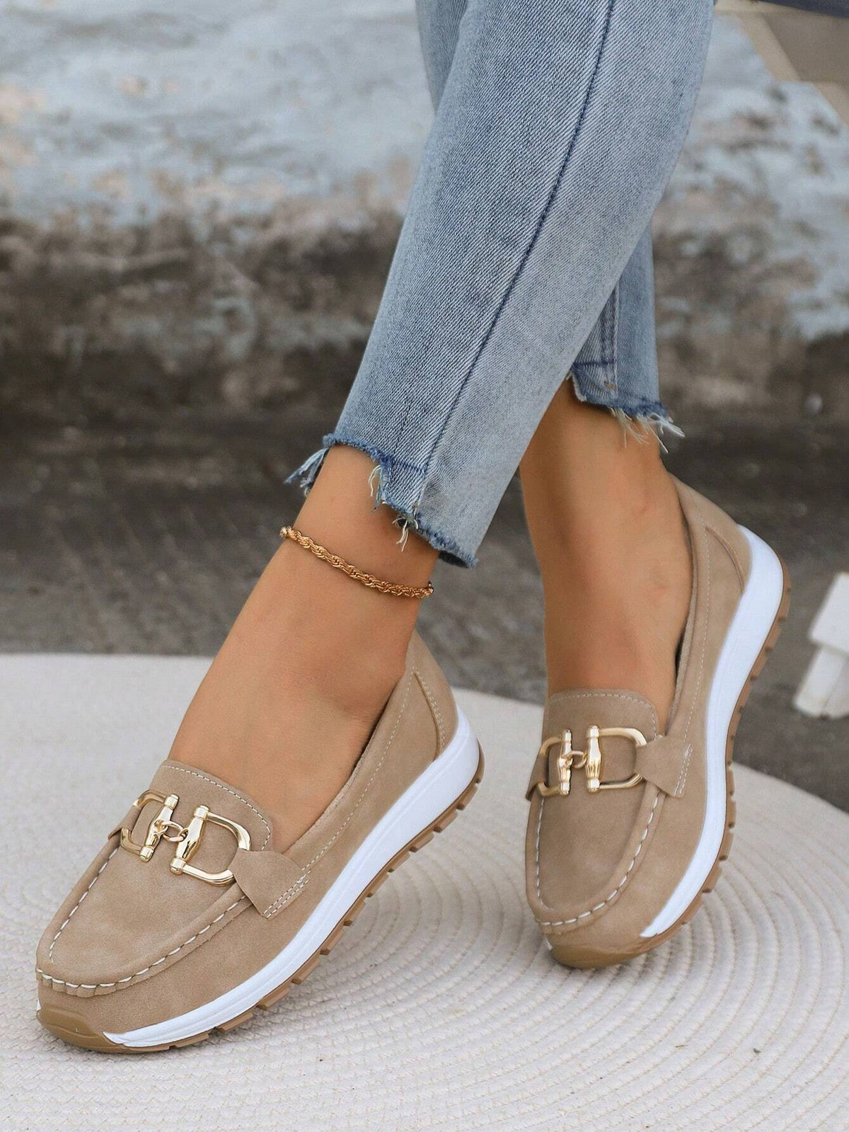 Pareja de mocasines beige con pespuntes visibles, plataforma deportiva y adorno metálico en una vista frontal inclinada.