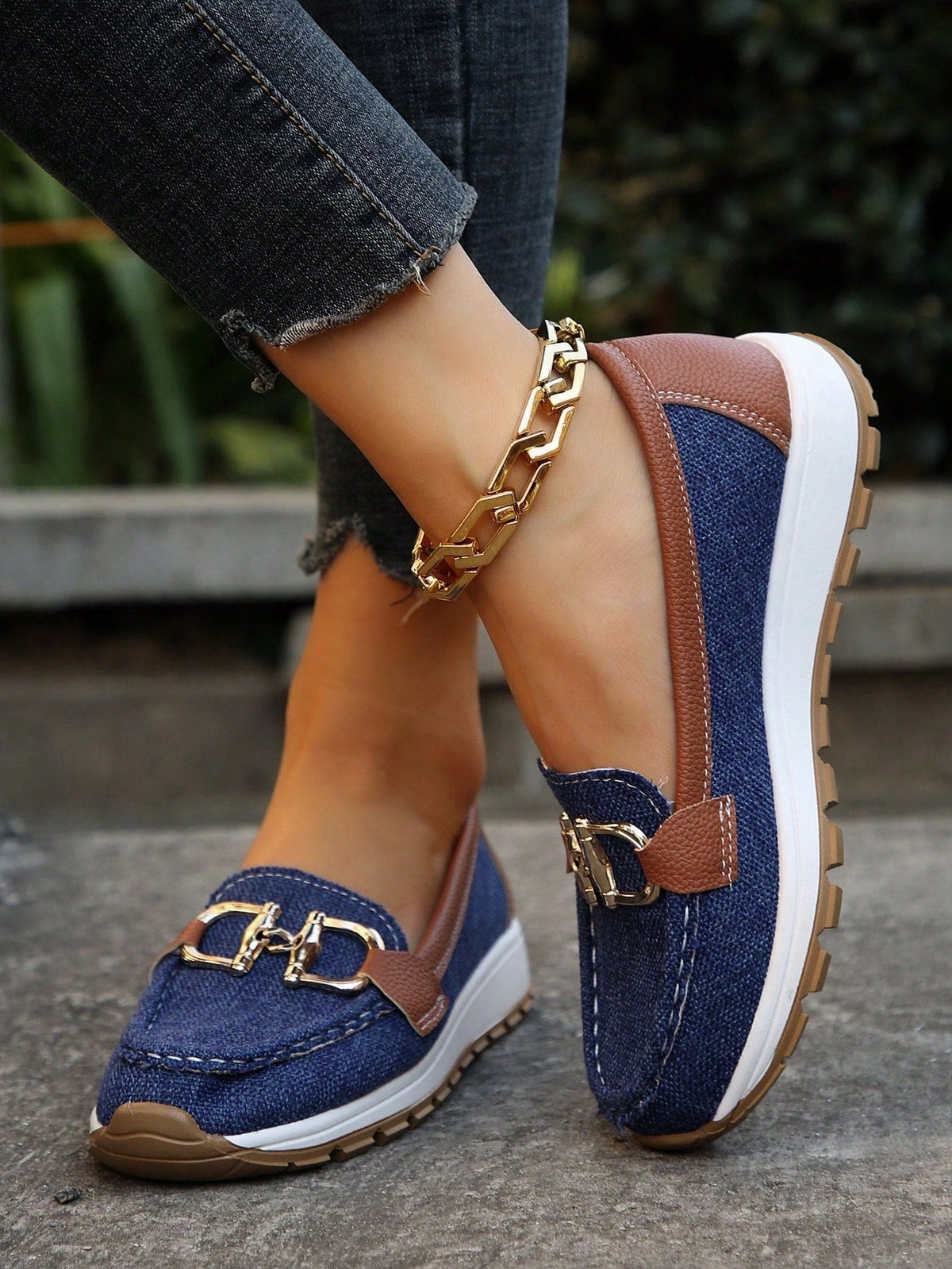 Mocasines azul oscuro con paneles marrones, plataforma blanca, suela dentada y adorno metálico en el empeine.