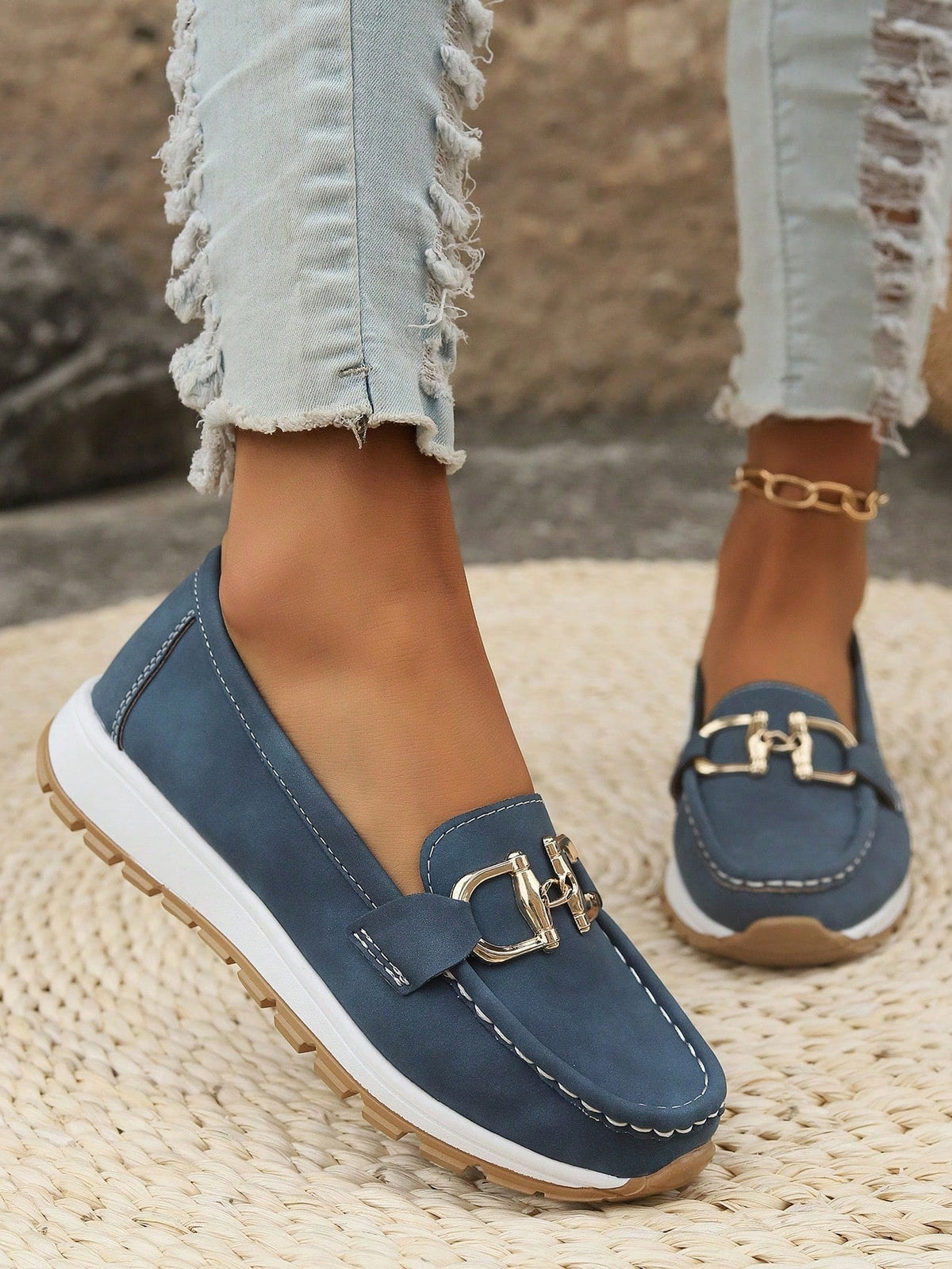 Mocasín azul oscuro en primer plano, con costuras claras, plataforma blanca y herraje metálico dorado.