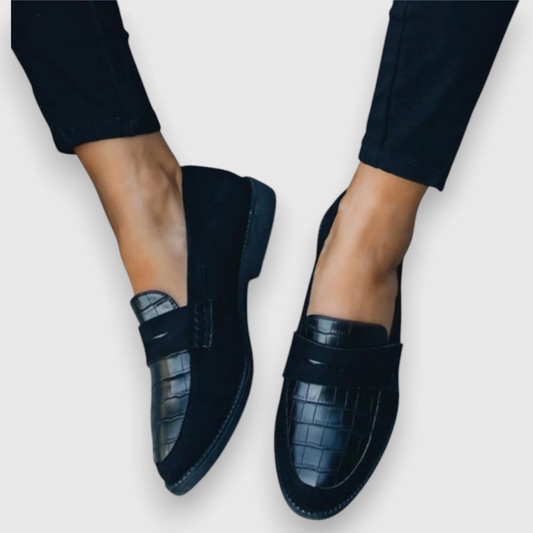 Mocasines negros de mujer con relieve de efecto cocodrilo en la puntera, banda frontal y tacón bajo, vistos desde arriba en ángulo.