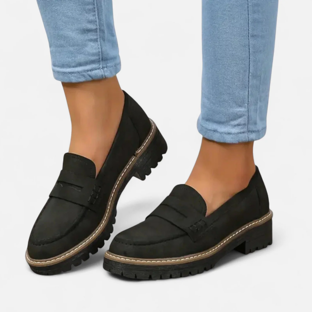 Mocasines negros de mujer con empeine clásico, pespuntes en contraste y suela gruesa dentada, combinados con vaqueros claros.