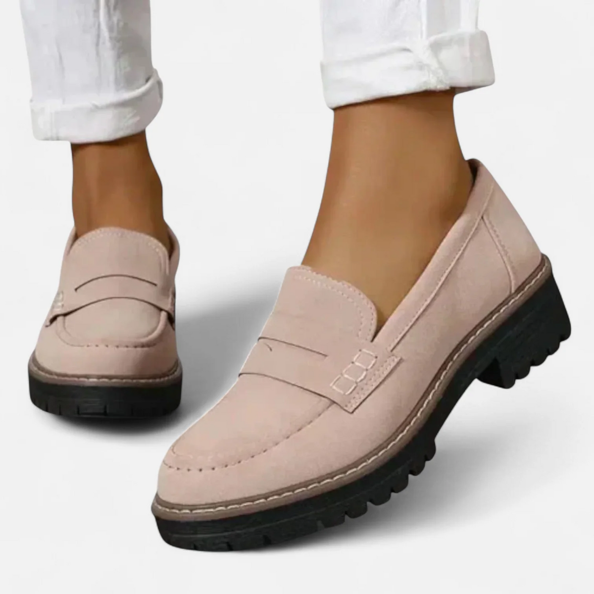 Mocasines rosa claro de mujer vistos de frente y en perspectiva, con detalle de tira sobre el empeine, pespuntes y suela negra de relieve marcado.