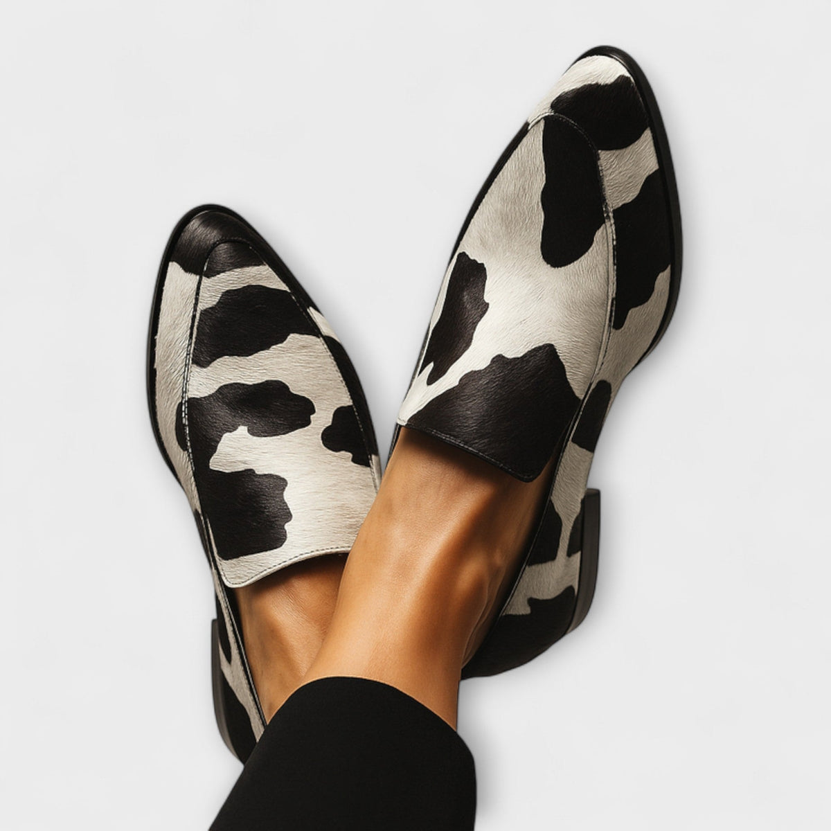 Mocasines de punta estilizada con estampado animal en blanco y negro, mostrados desde arriba y cruzados entre sí.