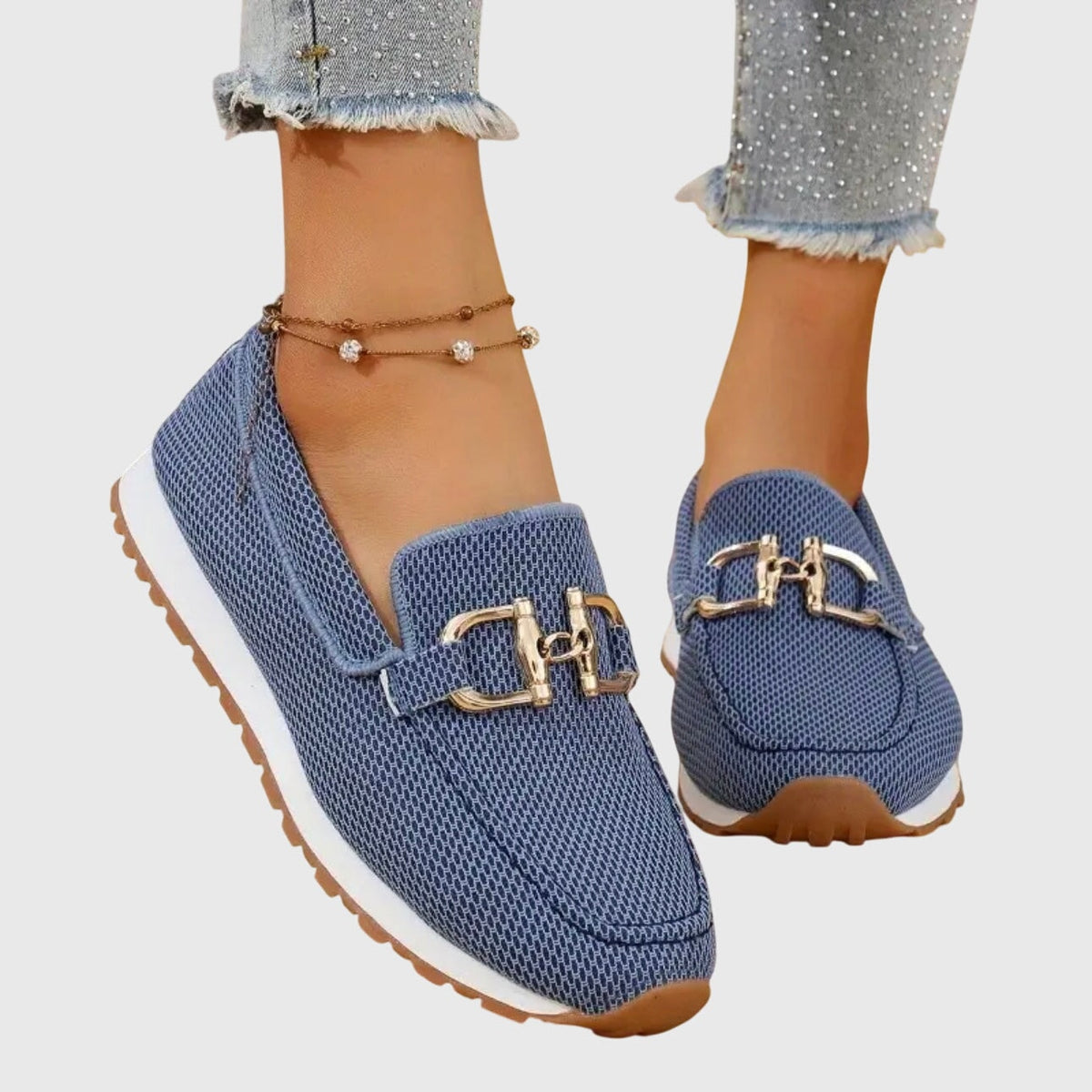Mocasines deportivos azules con adorno metálico dorado, vistos en los pies desde una perspectiva frontal elevada.
