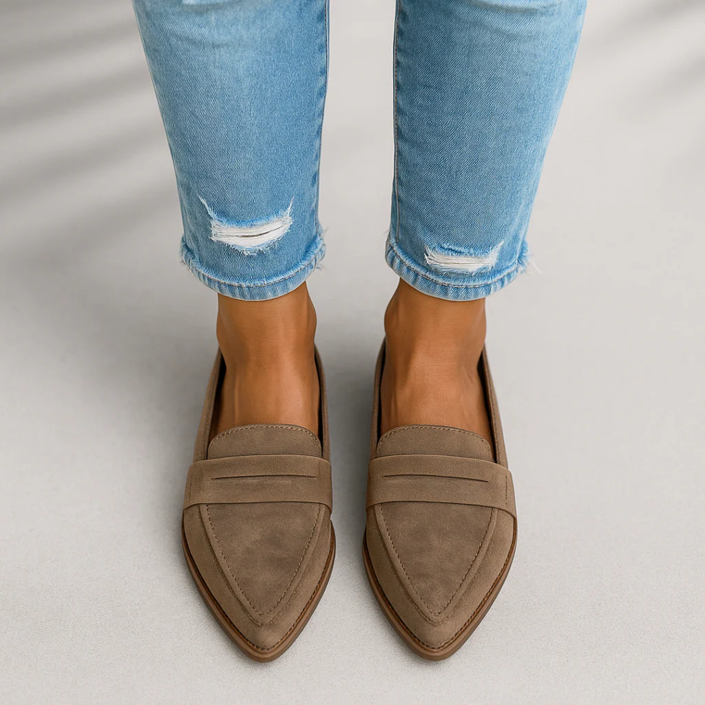 Mocasines planos taupe de punta afilada con pala clásica y banda decorativa, vistos desde arriba con vaqueros claros.