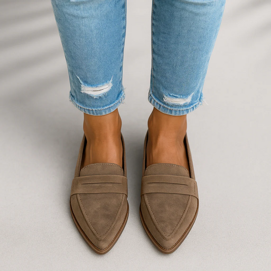 Mocasines planos taupe de punta afilada con pala clásica y banda decorativa, vistos desde arriba con vaqueros claros.