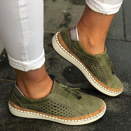 Mocasines planos verdes con laterales perforados, borlas decorativas y suela clara, vistos en los pies.
