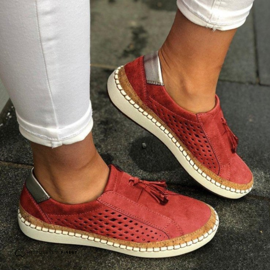 Mocasines planos rojos con paneles perforados, borlas en el empeine y suela clara.