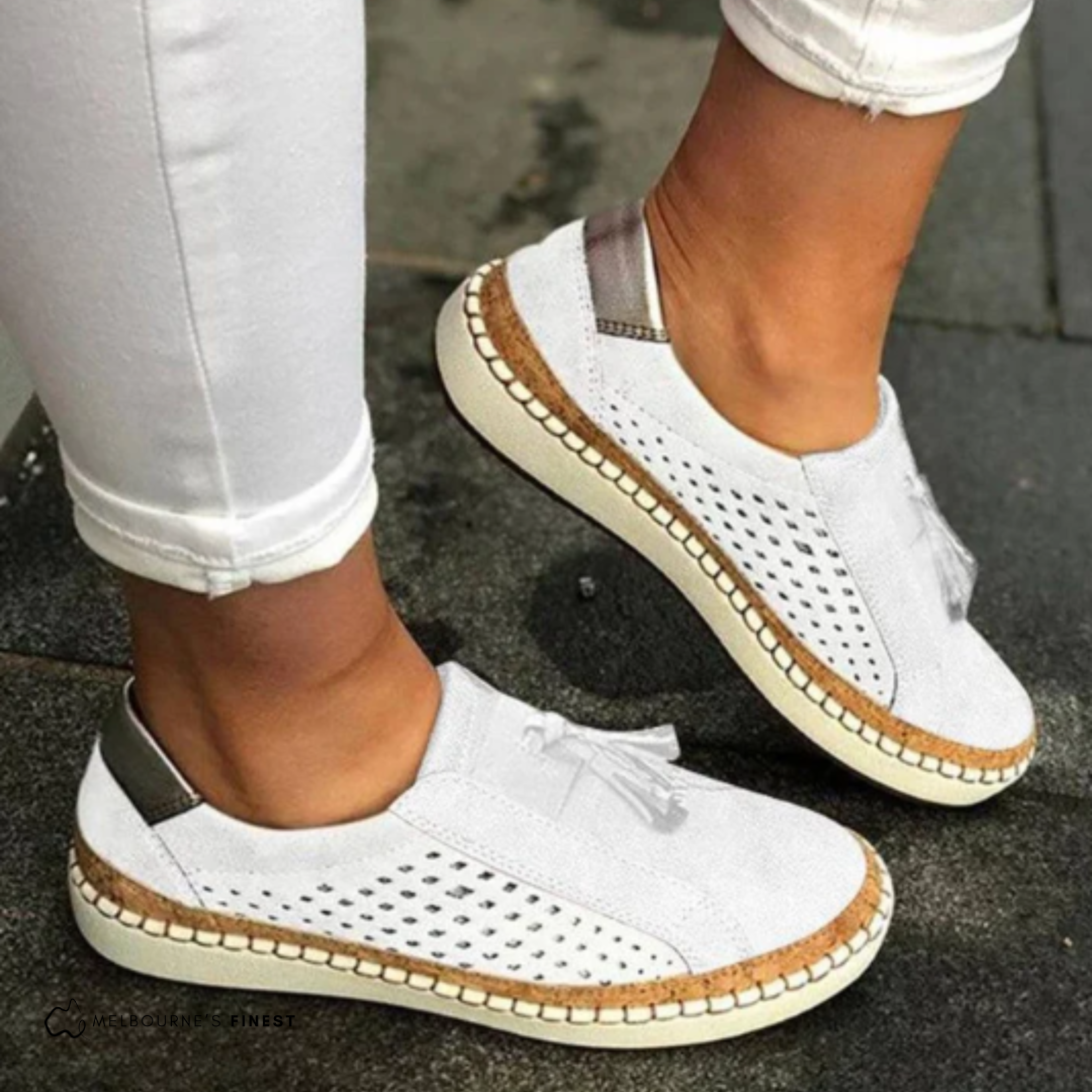 Mocasines planos blancos con perforaciones laterales, borlas y suela clara con detalle en tono marrón.
