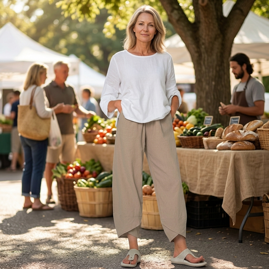 Pantalón cropped beige de pierna ancha con bajo asimétrico cruzado, visto de frente en un mercado al aire libre.