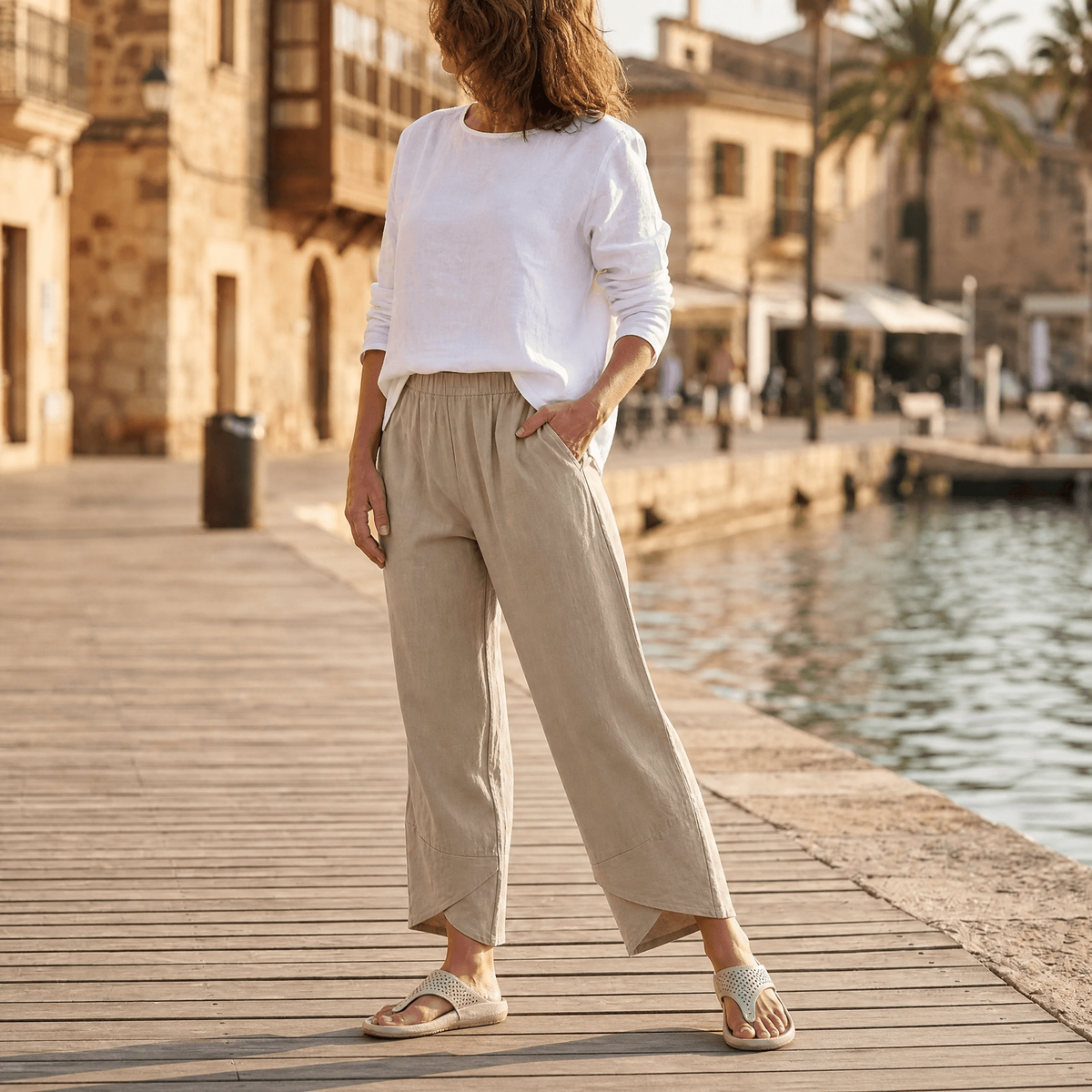 Vista frontal del pantalón cropped beige con pierna ancha y bajo asimétrico junto al agua.