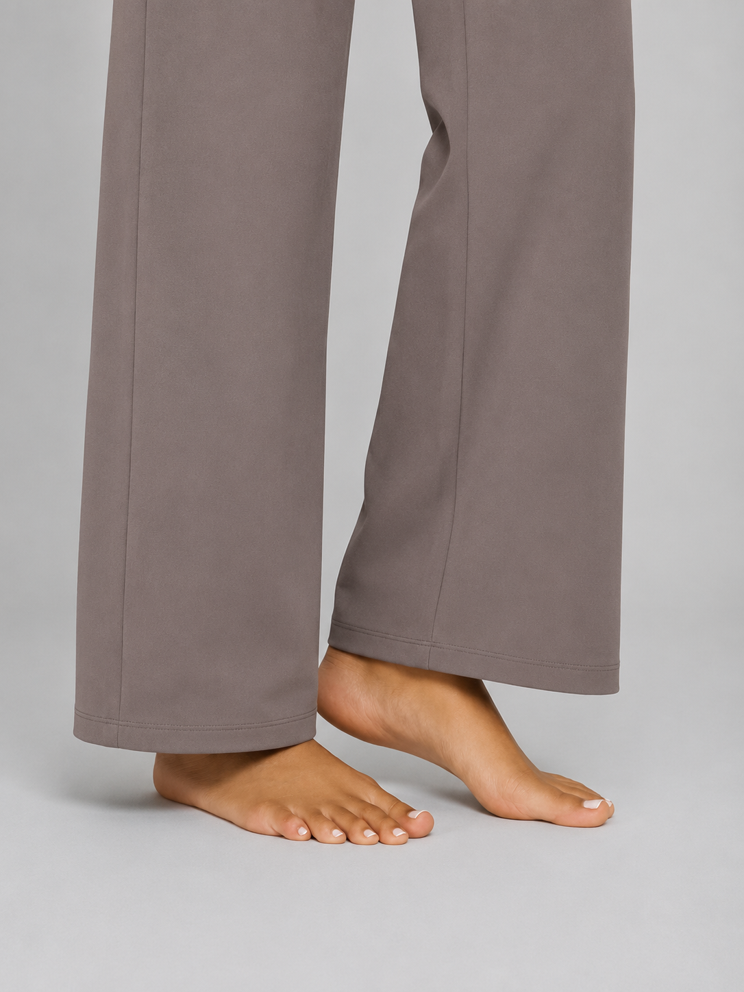 Detalle de los bajos amplios del pantalón topo y sus costuras, vistos junto a los pies descalzos.