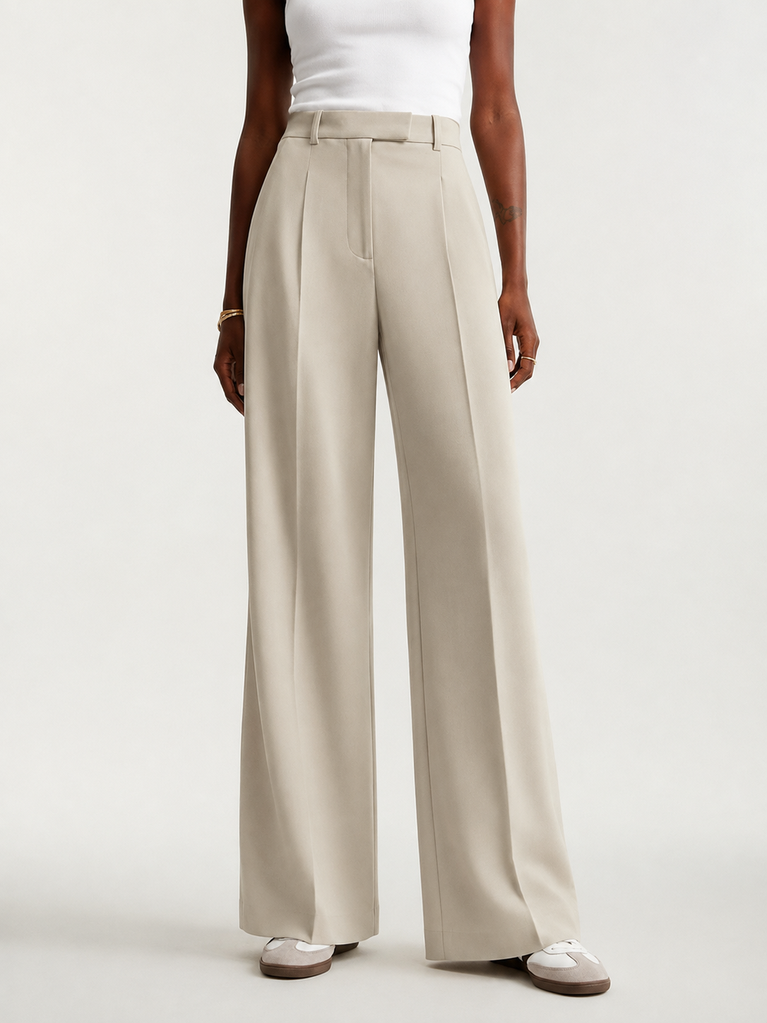 Pantalón de tiro alto color marfil con pinzas delanteras y pierna ancha, mostrado de frente con zapatillas.