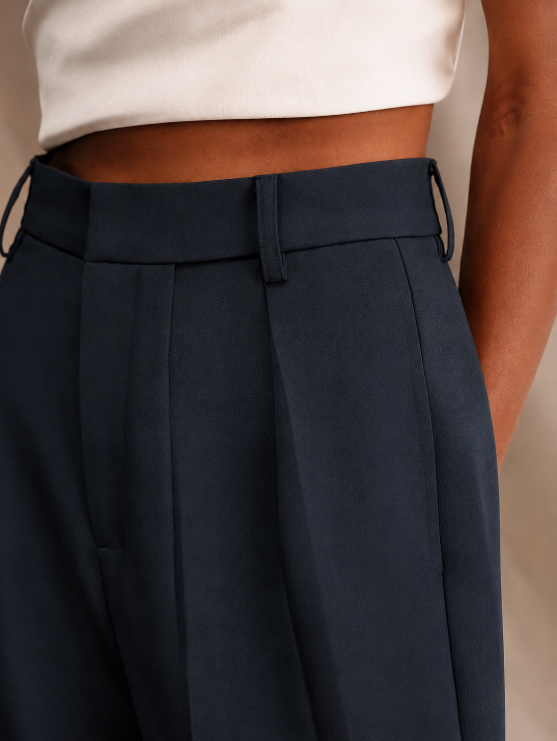 Detalle cercano del pantalón azul marino con cinturilla, trabillas y pinzas delanteras.