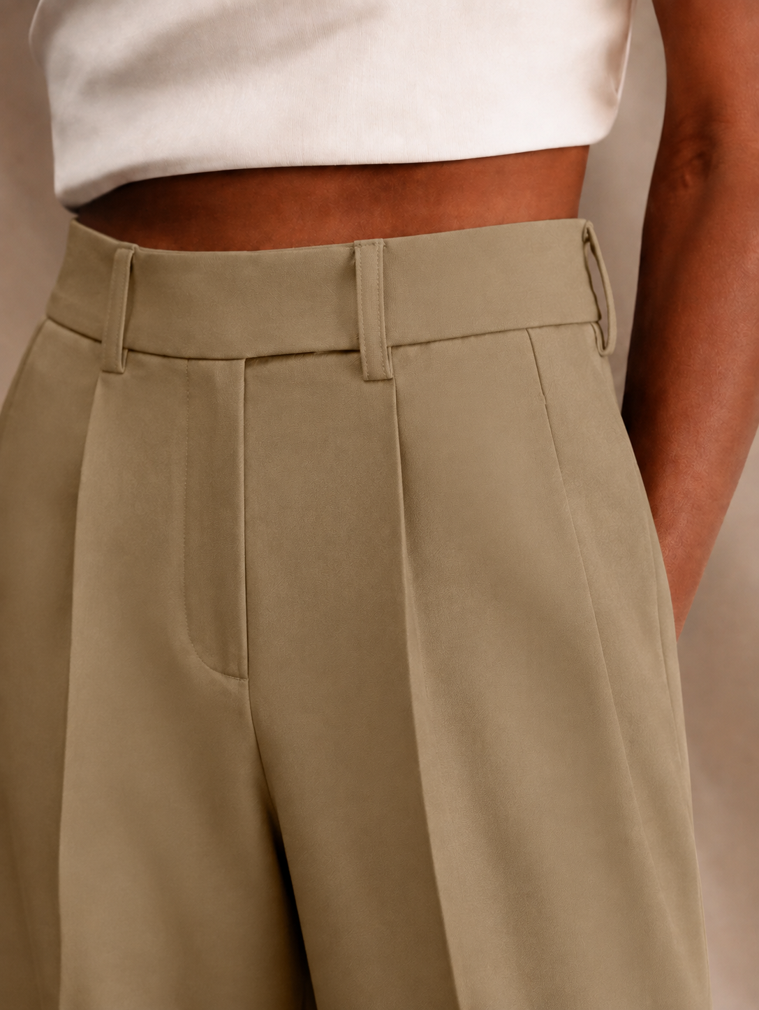 Detalle del pantalón beige con tiro alto, trabillas y pliegue delantero definido.