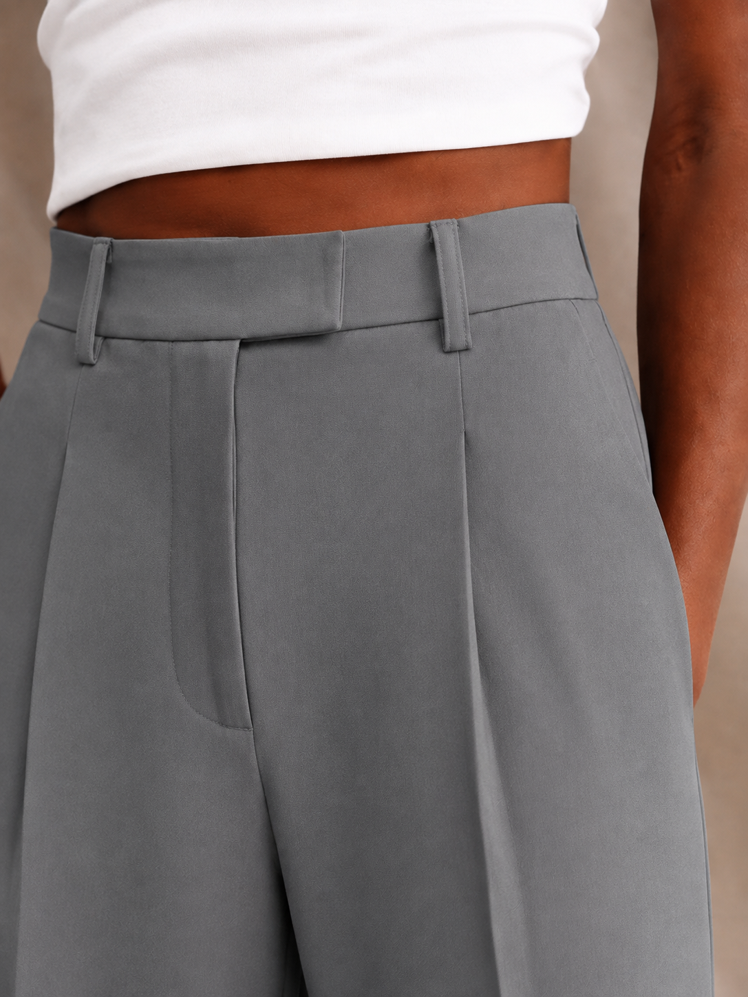 Primer plano del pantalón gris con cinturilla estructurada, trabillas y pinza frontal.