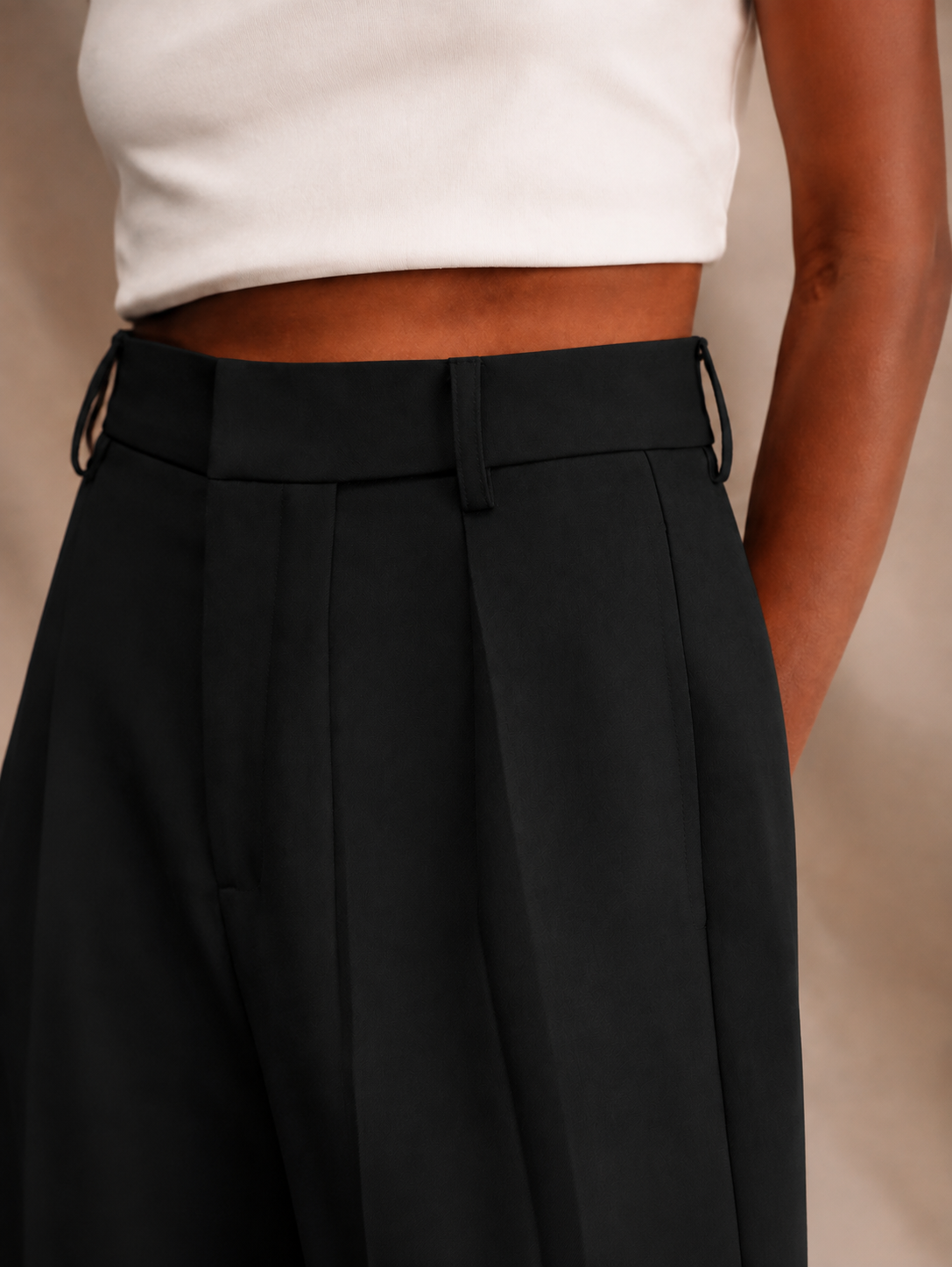 Primer plano del pantalón negro con trabillas laterales, pinzas delanteras y bolsillo visible.