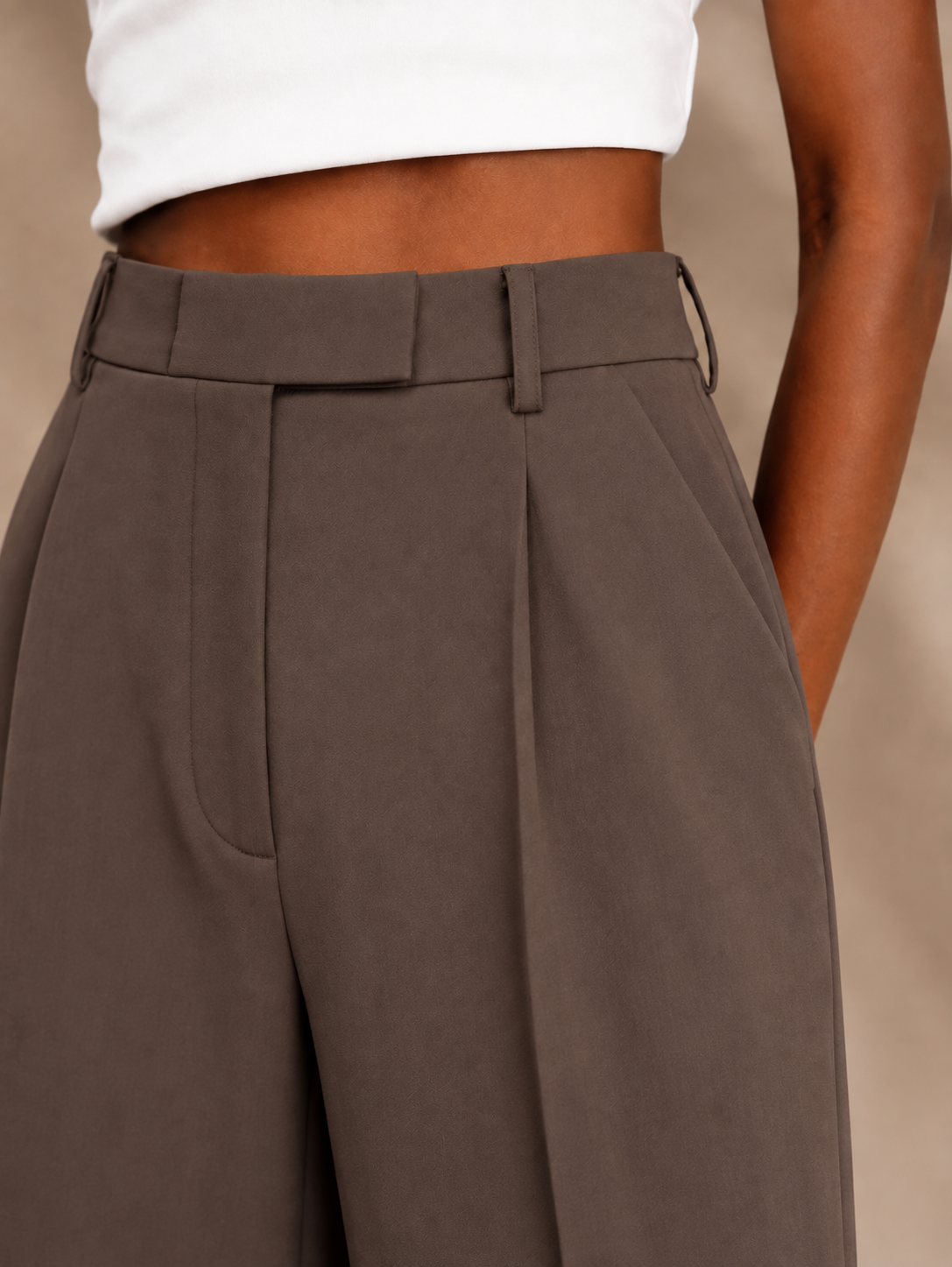 Detalle cercano del pantalón marrón topo con cinturilla alta y pinza frontal marcada.